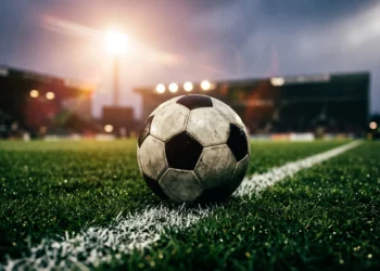 A soccer ball on a pitch under stadium lights.