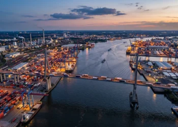 A long bridge connecting two industrial cities across a river at sunset.